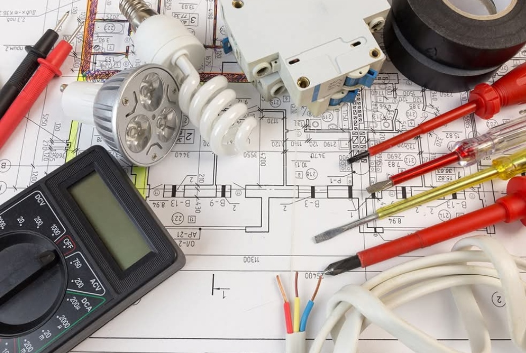 Electrician's tools and a multimeter laid over electrical plans